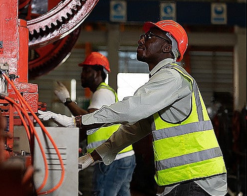 Workers in a factory setting with machinery and safety gear.